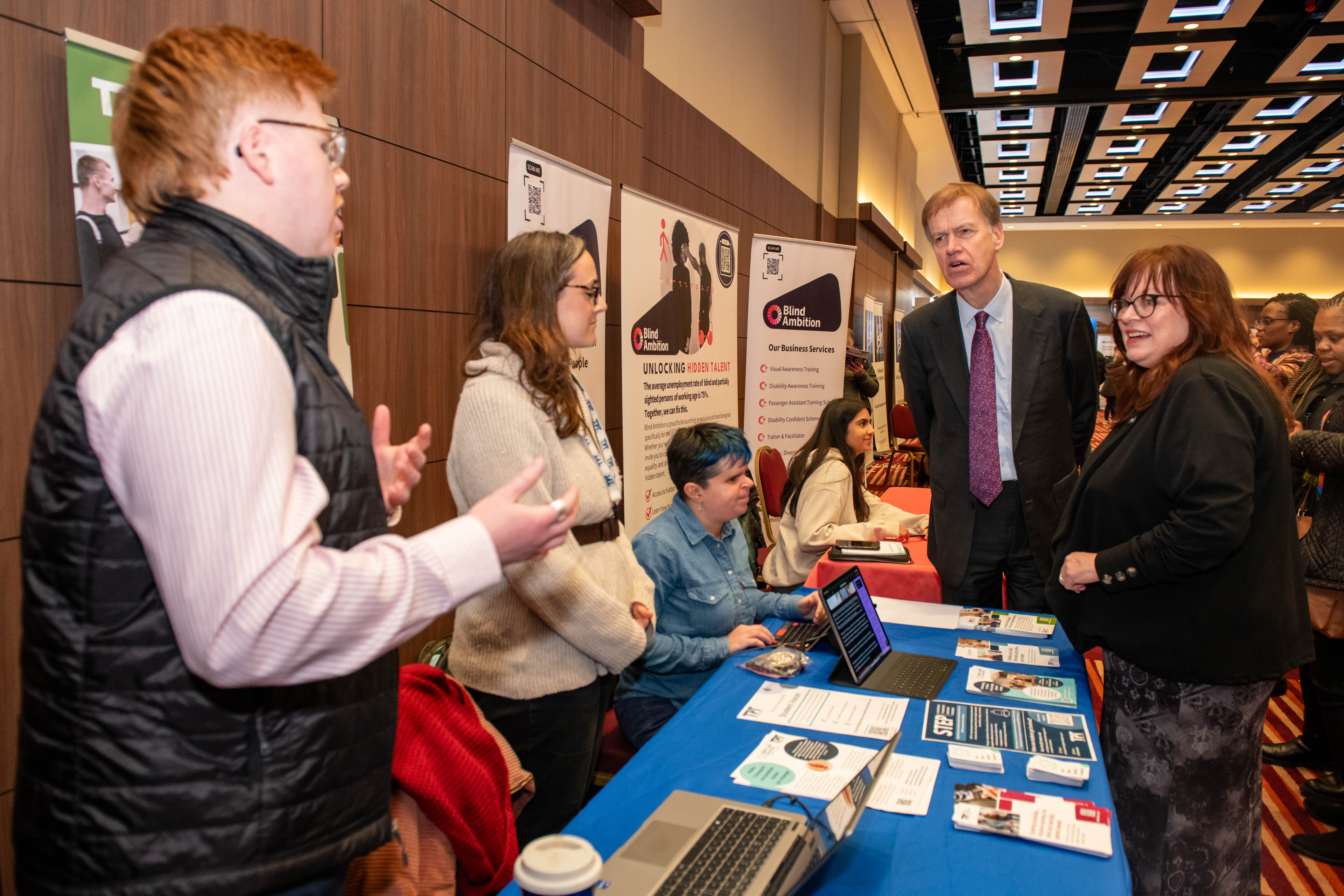 Bev and Stephen listening to two exhibitors next to a table of information Bev and Stephen listening to two exhibitors next to a table of information