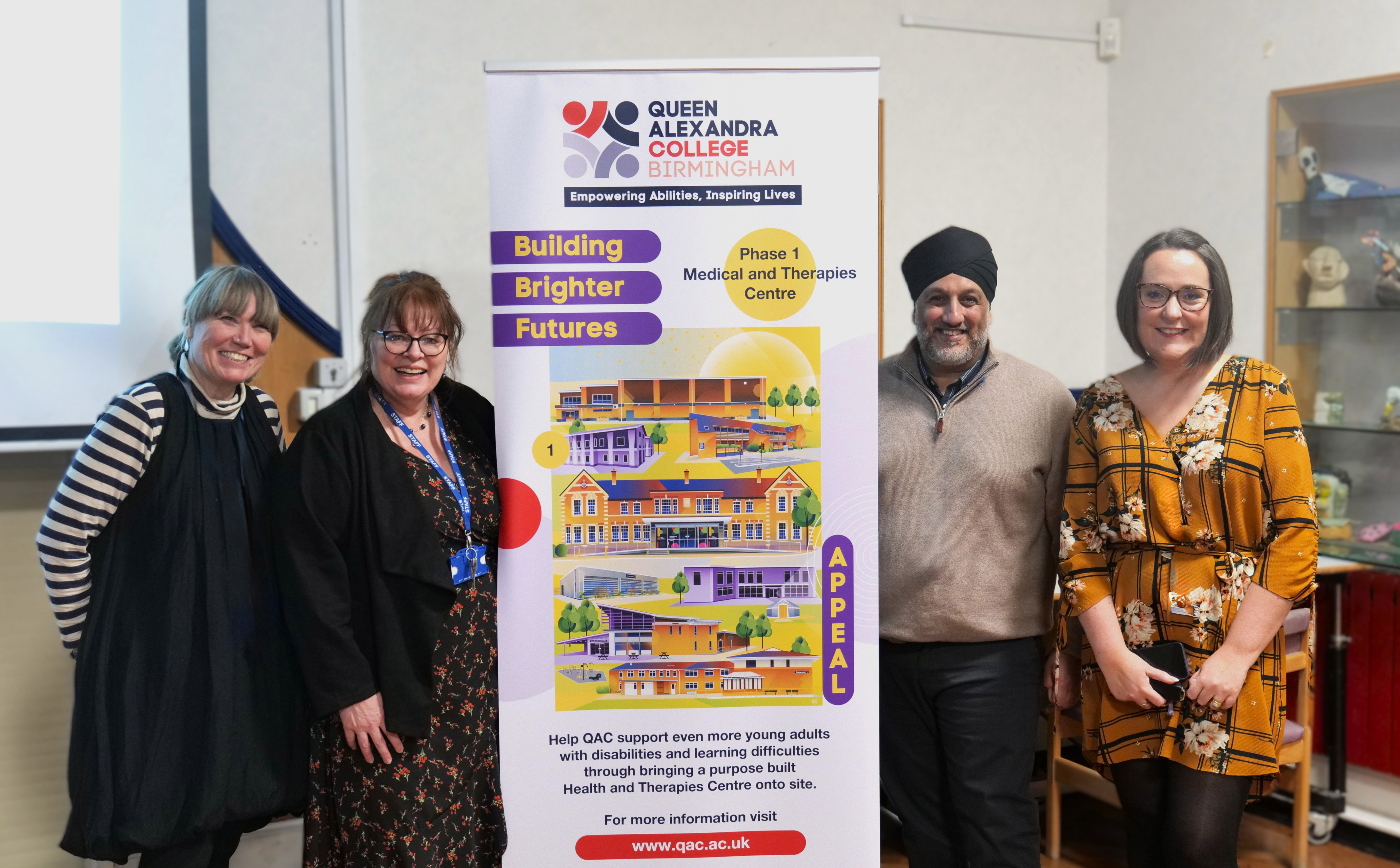 Image of 4 QAC staff members stood next to the Building Brighter Futures Banner