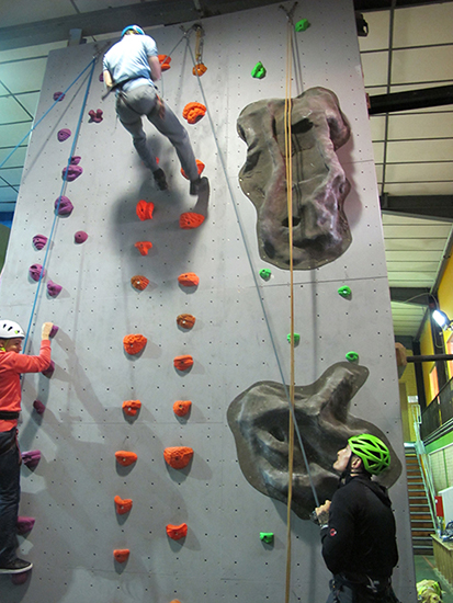 2 students climbing a climbing wall with someone supervising at the bottom 2 students climbing a climbing wall with someone supervising at the bottom
