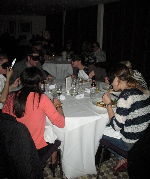 Diners sat wearing blindfolds eating around a table