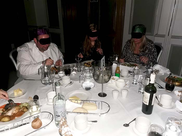 Another group of individuals sat enjoying a meal at Dinner in the Dark whilst wearing blindfolds