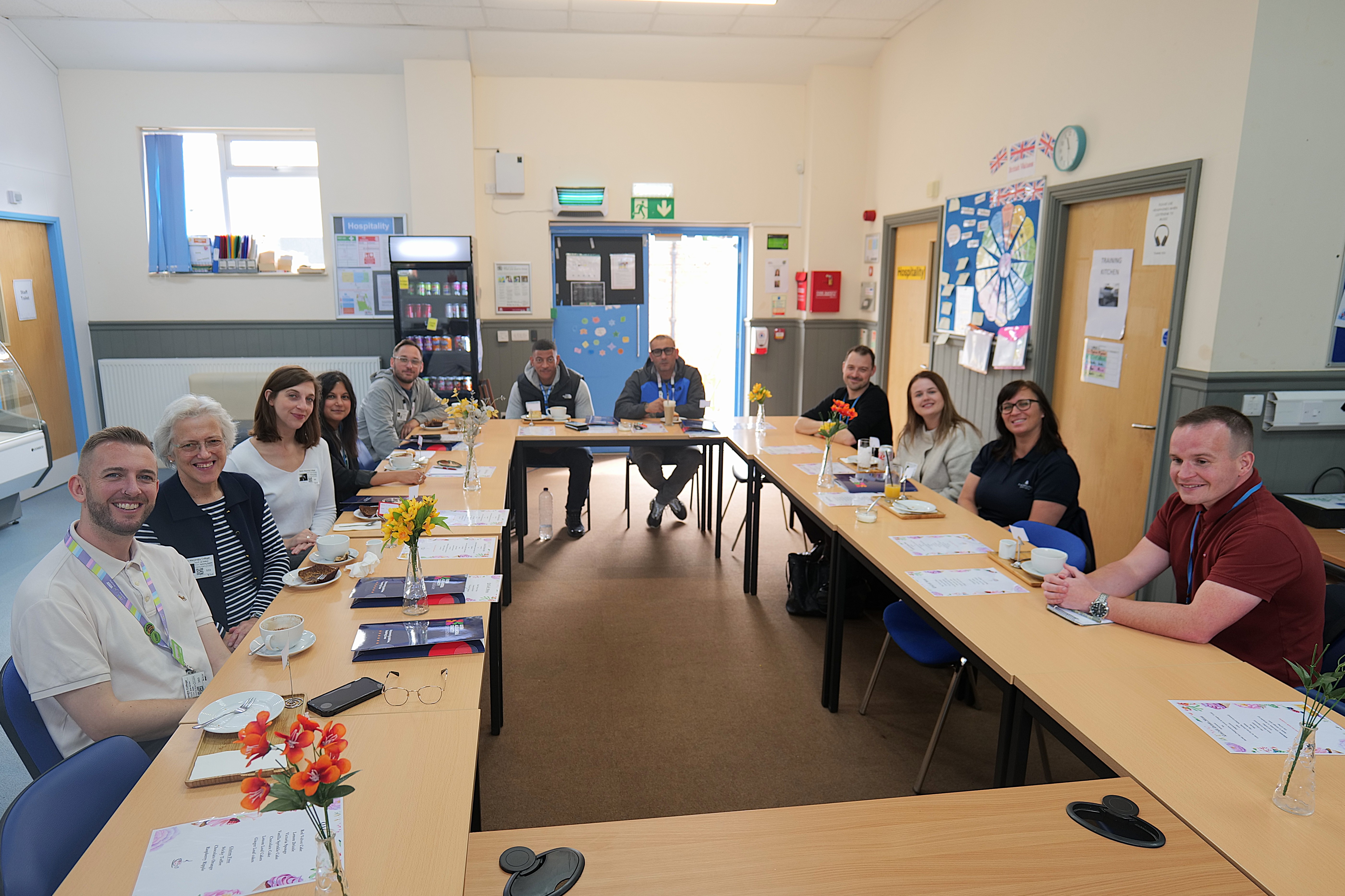 Image of Employees and QAC staff sat around a table smiling Image of Employees and QAC staff sat around a table smiling