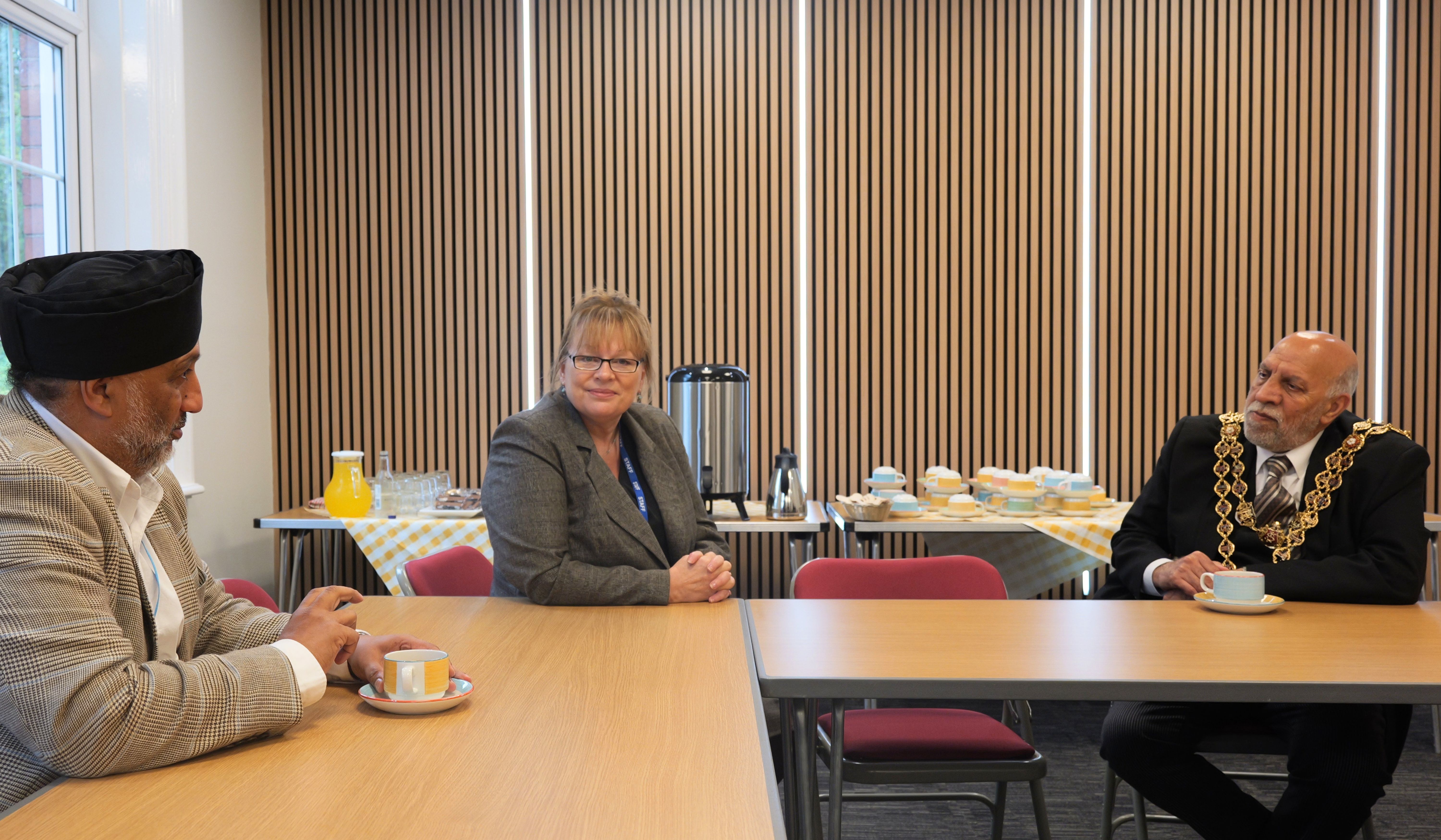 Three people seated around tables during a meeting with refreshments in the background Three people seated around tables during a meeting with refreshments in the background