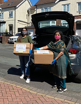 Photo of Manisha and another lady holding donation boxes, both wearing face masks.