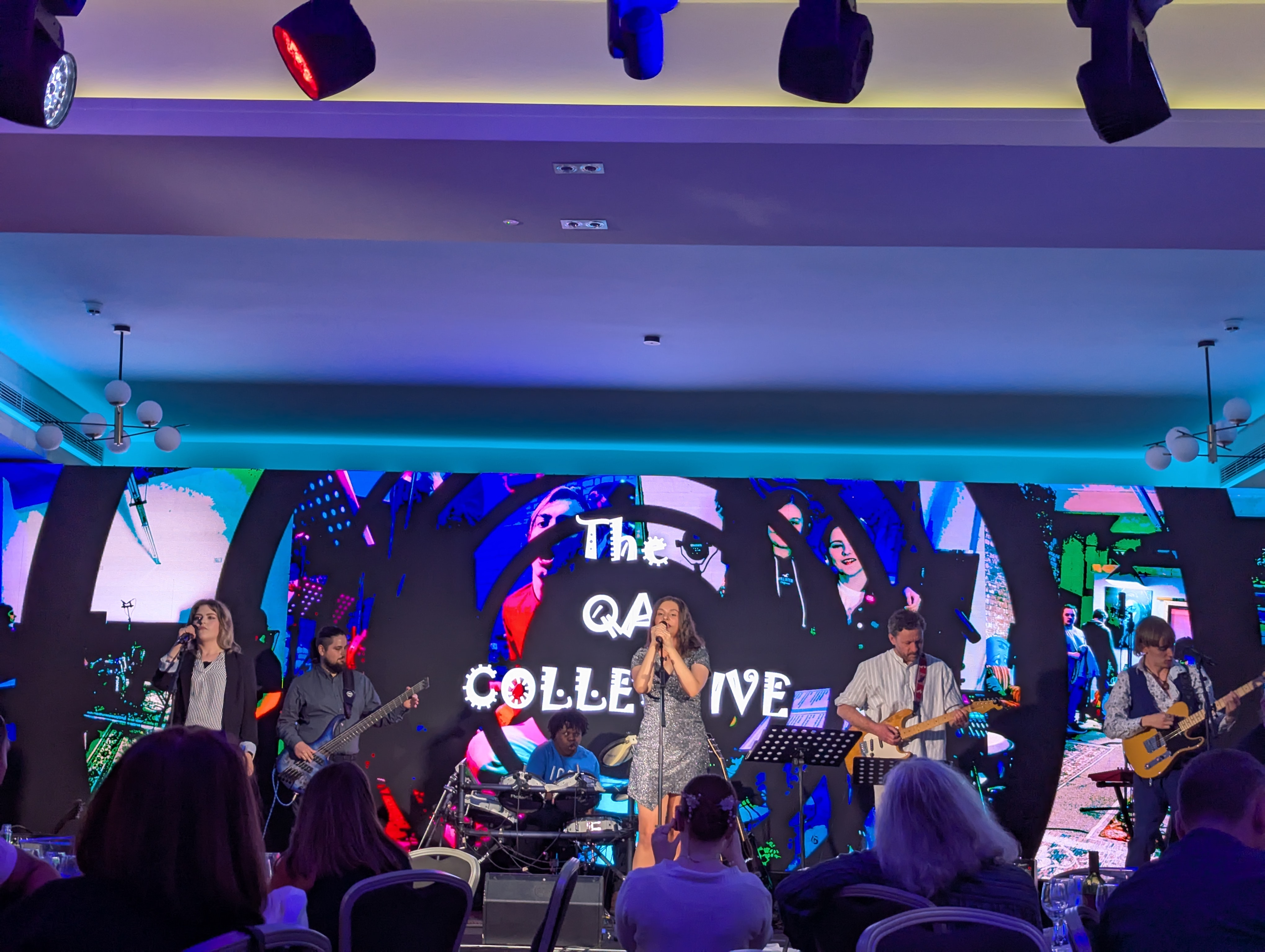 QA Collective performing on stage with a photo in the background 