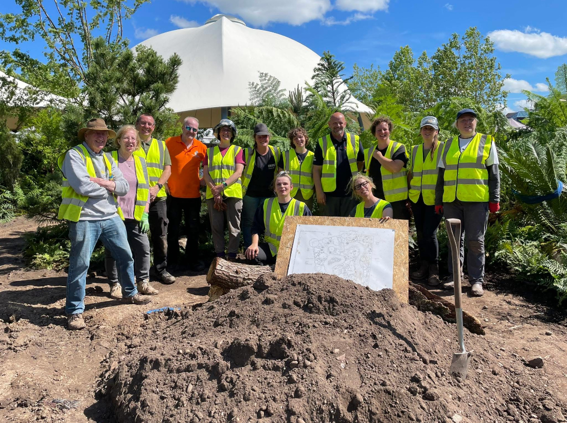 A large group of people wearing high-visibility yellow vests stand together outdoors at a garden construction site at the NEC A large group of people wearing high-visibility yellow vests stand together outdoors at a garden construction site at the NEC