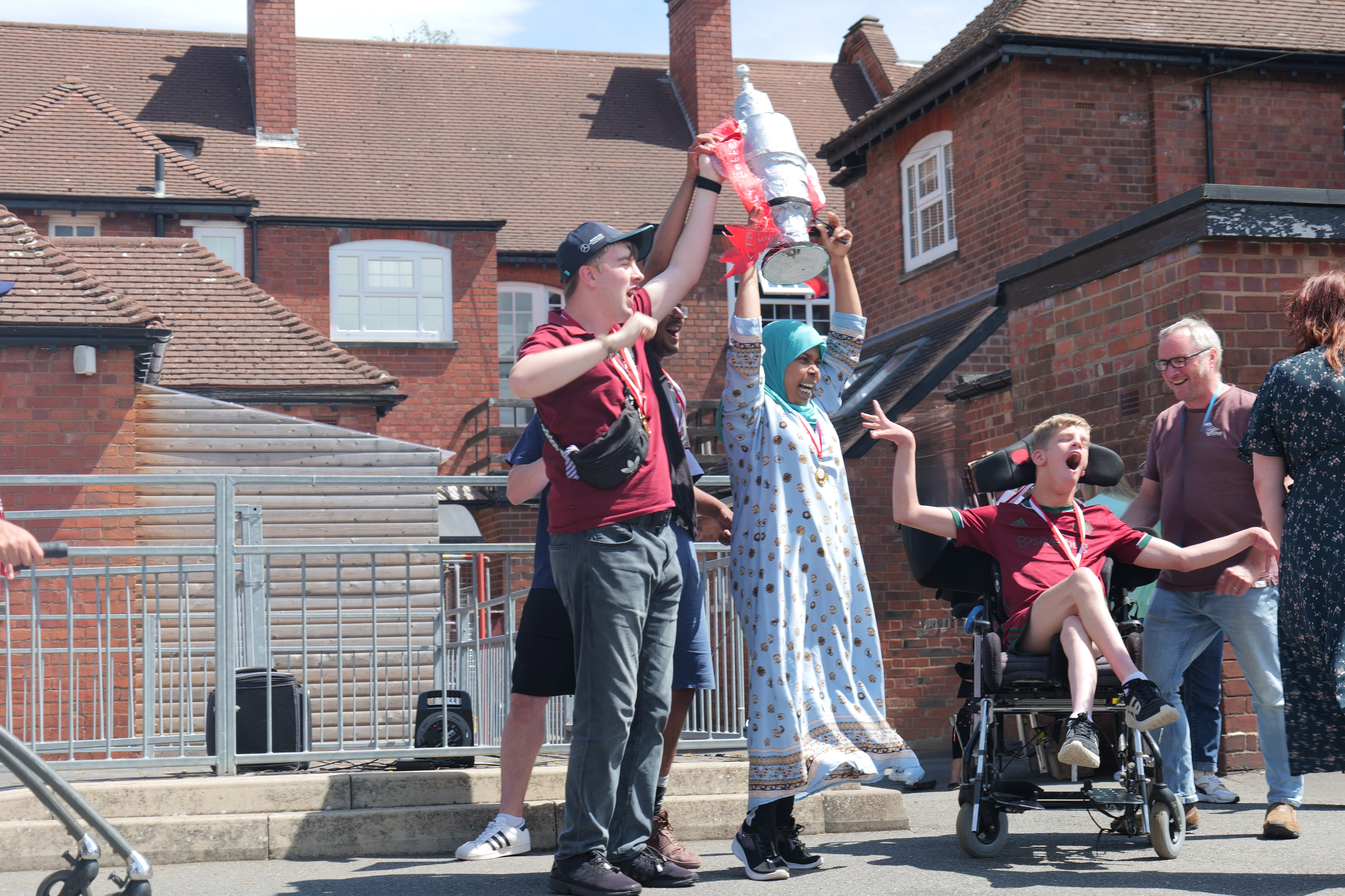 Image of 4 students holding a life size trophy in the air and cheering 