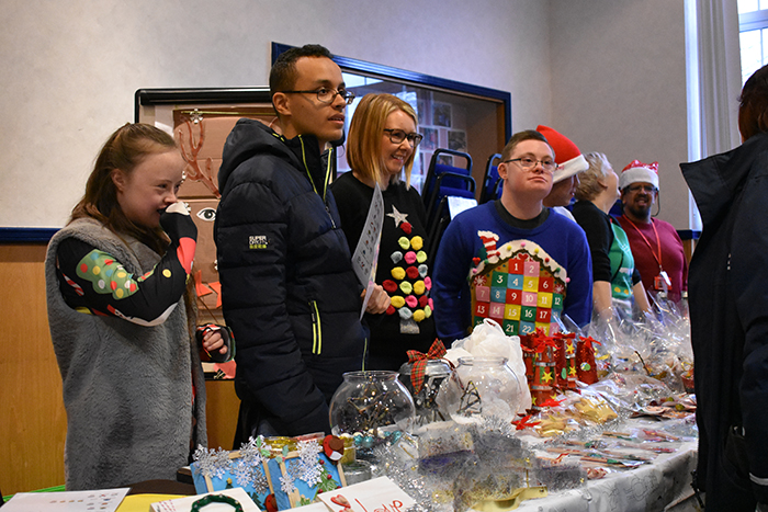 Students and staff stood behind a stall at the Christmas Fayre, serving a customre