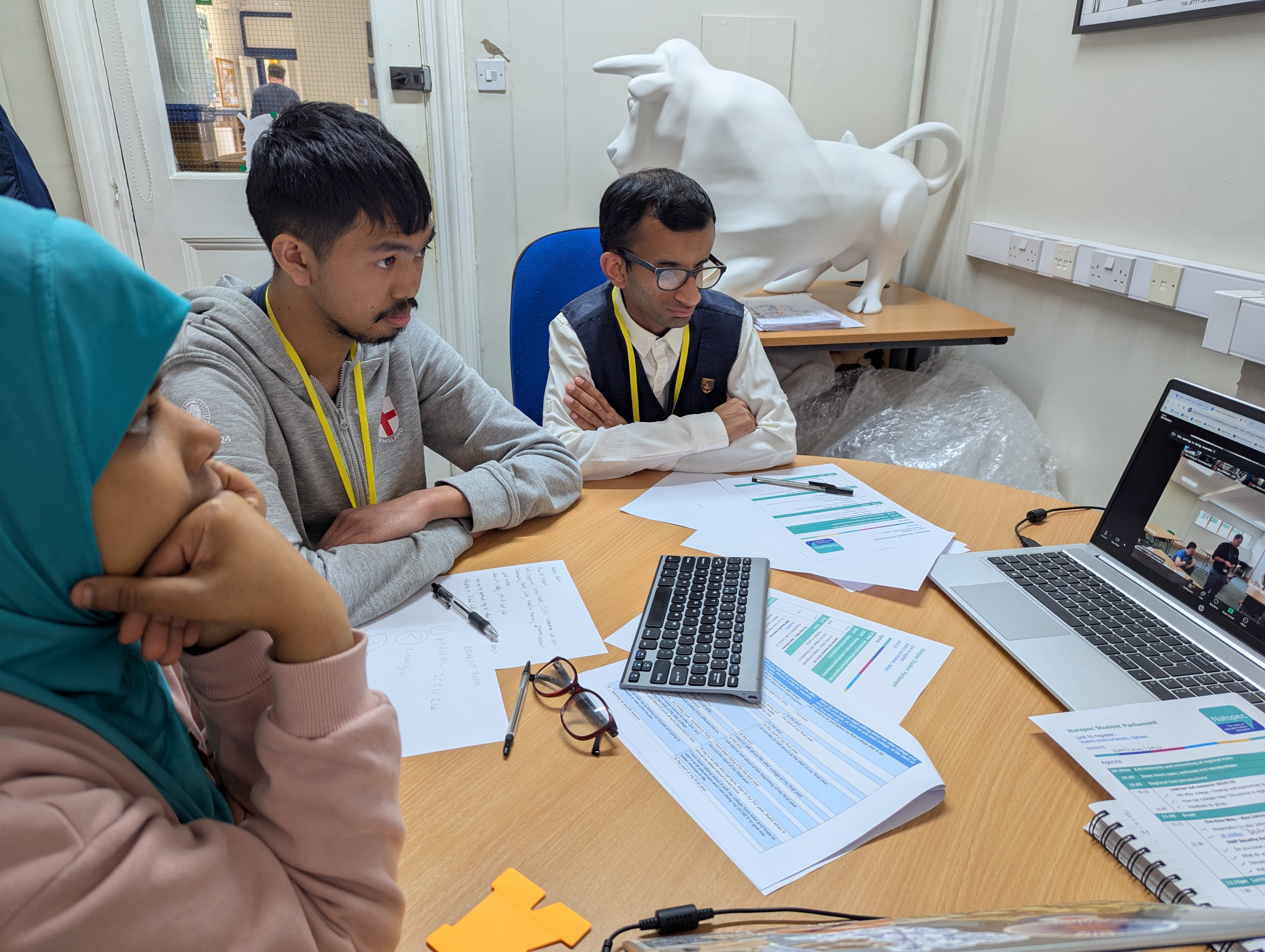Image of three QAC students sat at a table looking at a zoom call