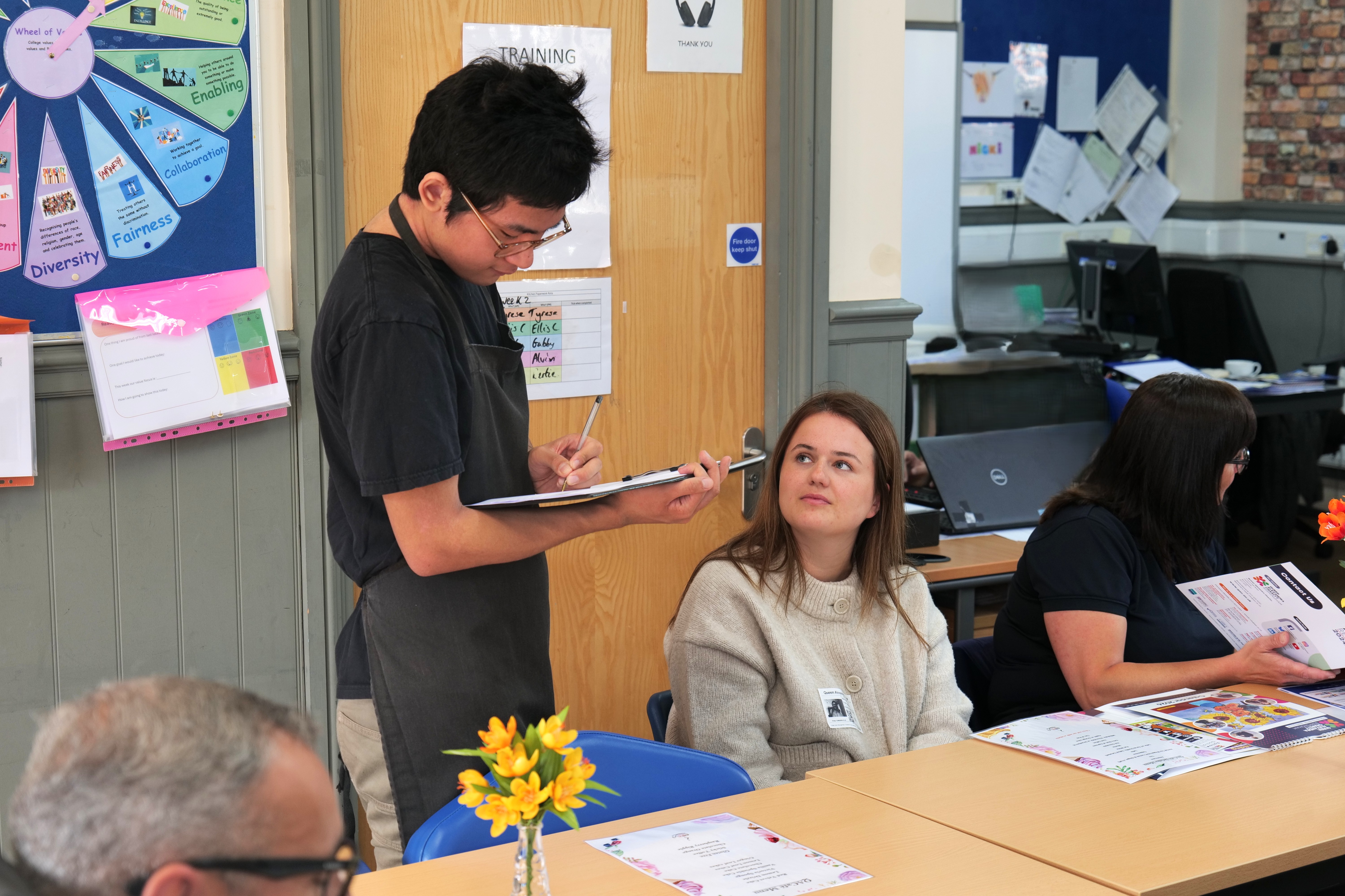 Student serving a visitor using a clipboard. Student serving a visitor using a clipboard.