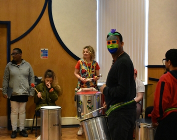 QAC Student in a Mardi Gras mask playing drum