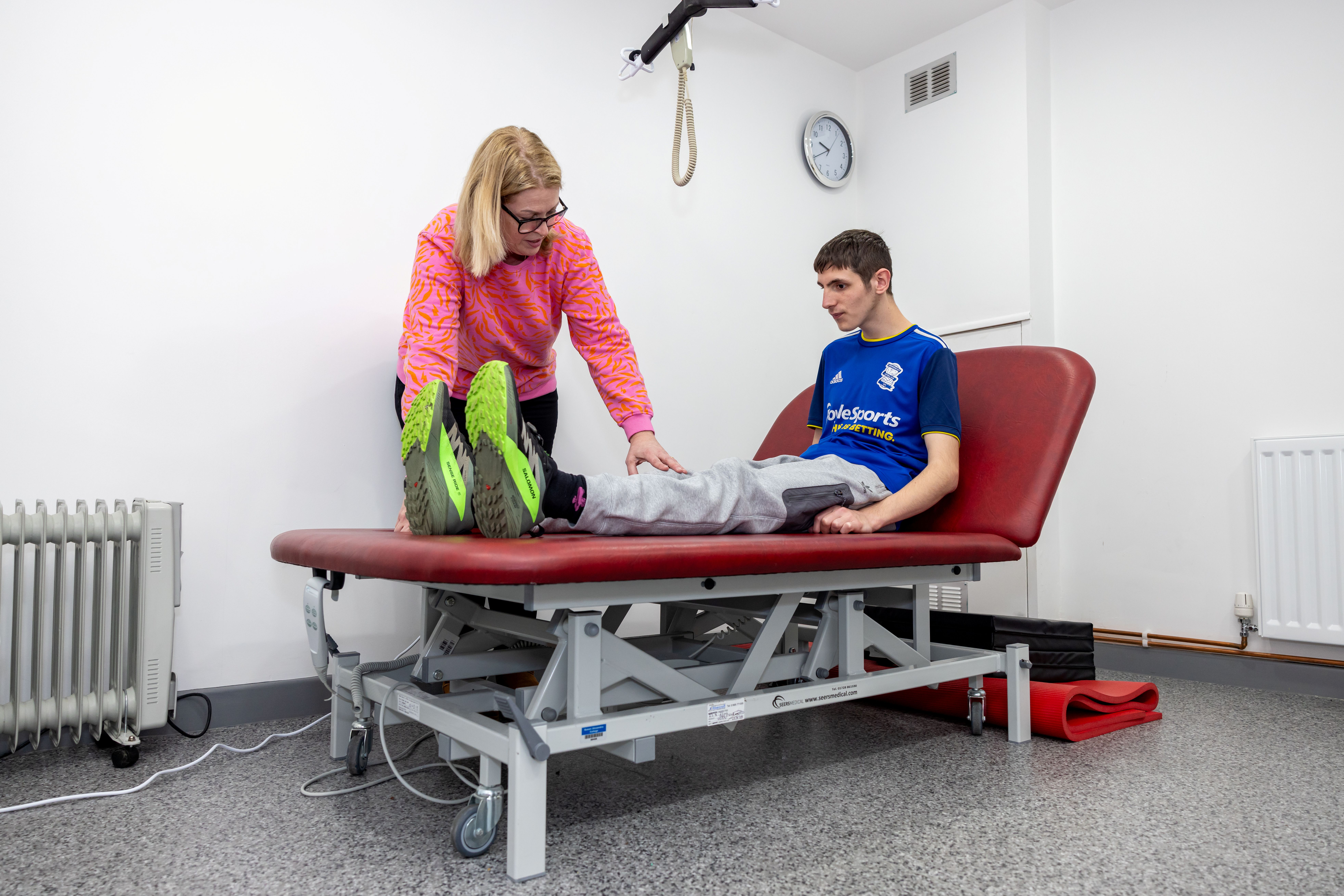 A student sat on a physio bed with staff assessing